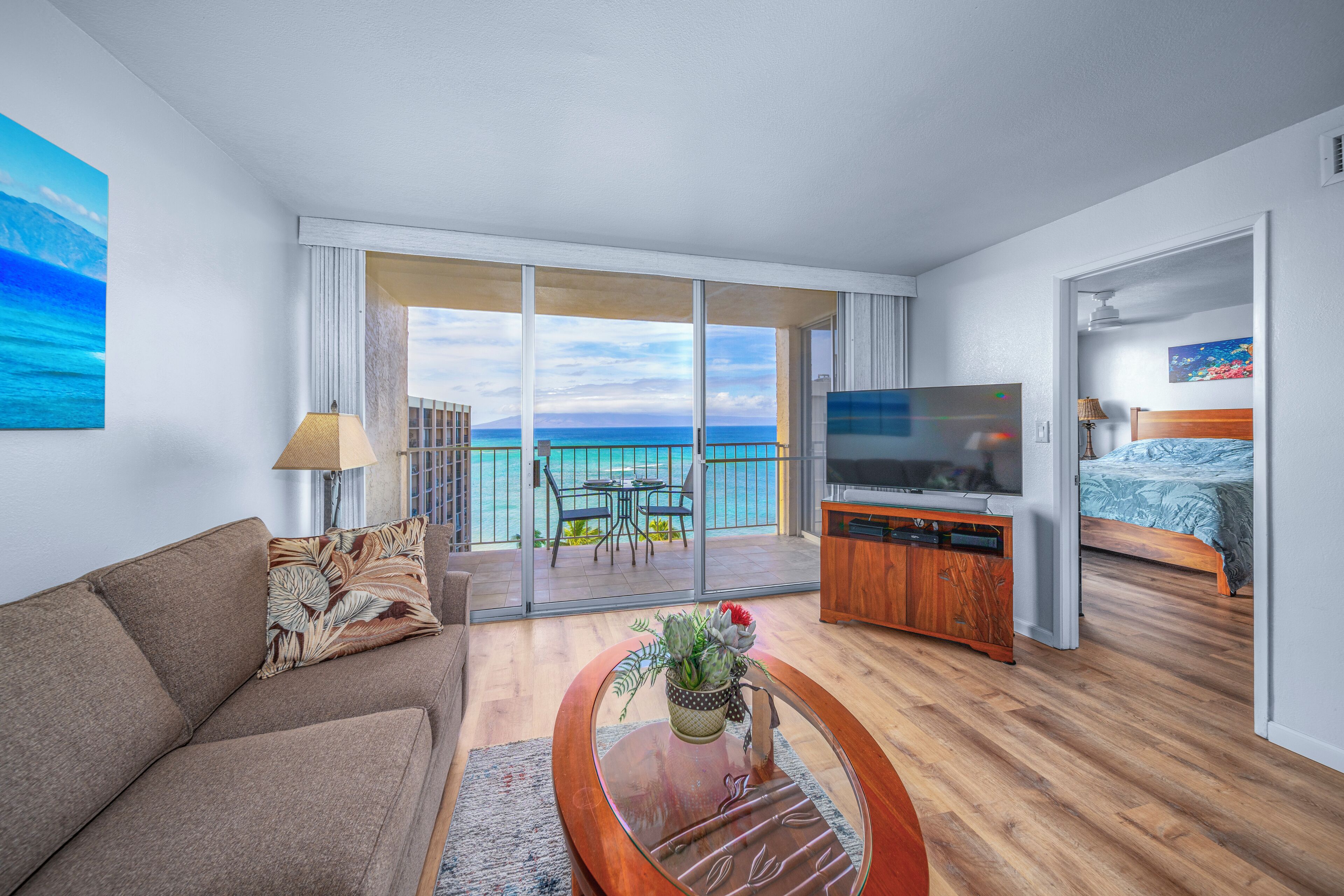 A modern hotel room with a balcony, a sofa, a coffee table with a vase, a TV, and a bed.