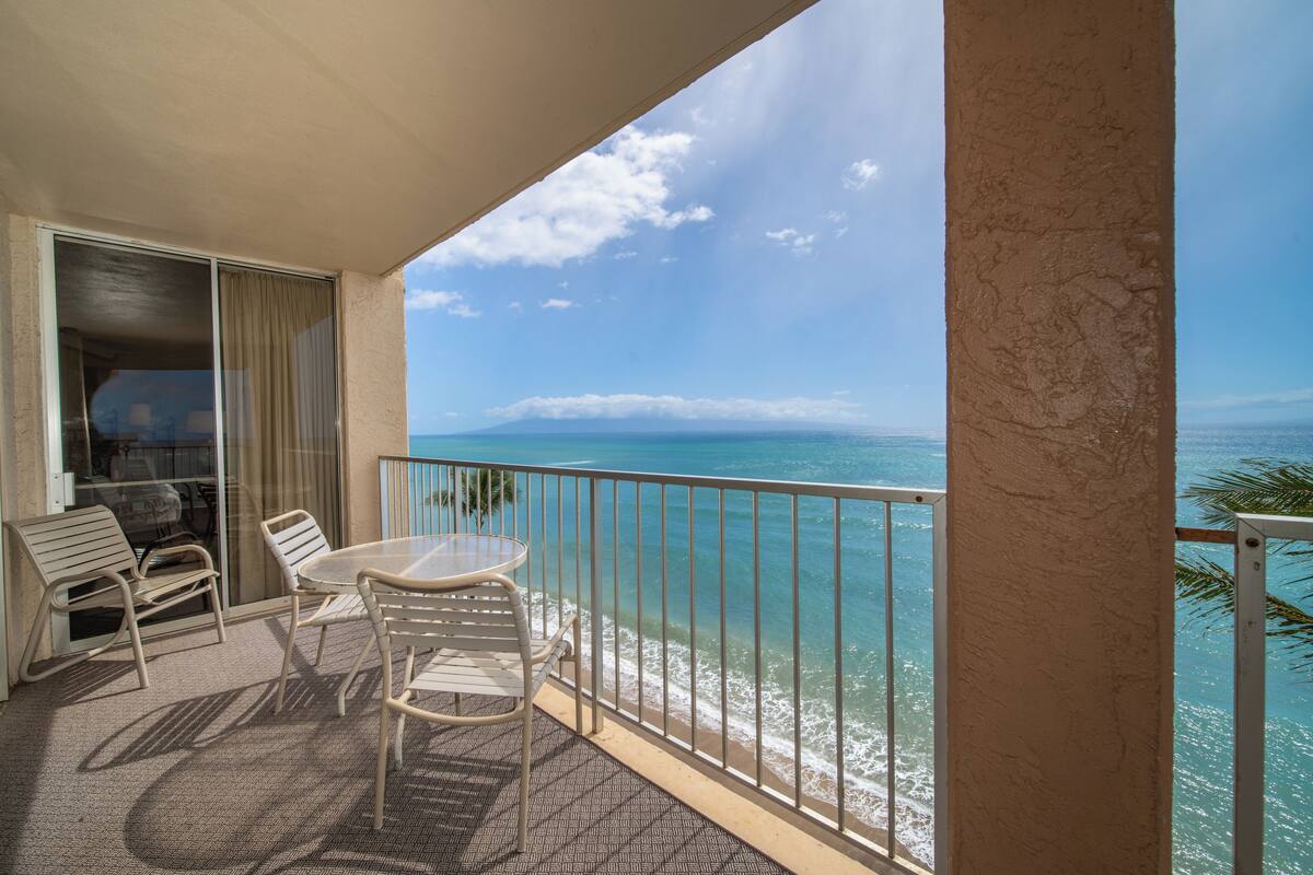A balcony with a view of the ocean, a table, and two chairs.