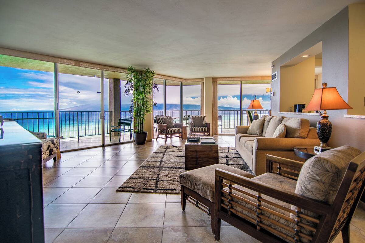 A spacious living room with a large window overlooking the ocean, furnished with a sofa, chairs, and a coffee table.
