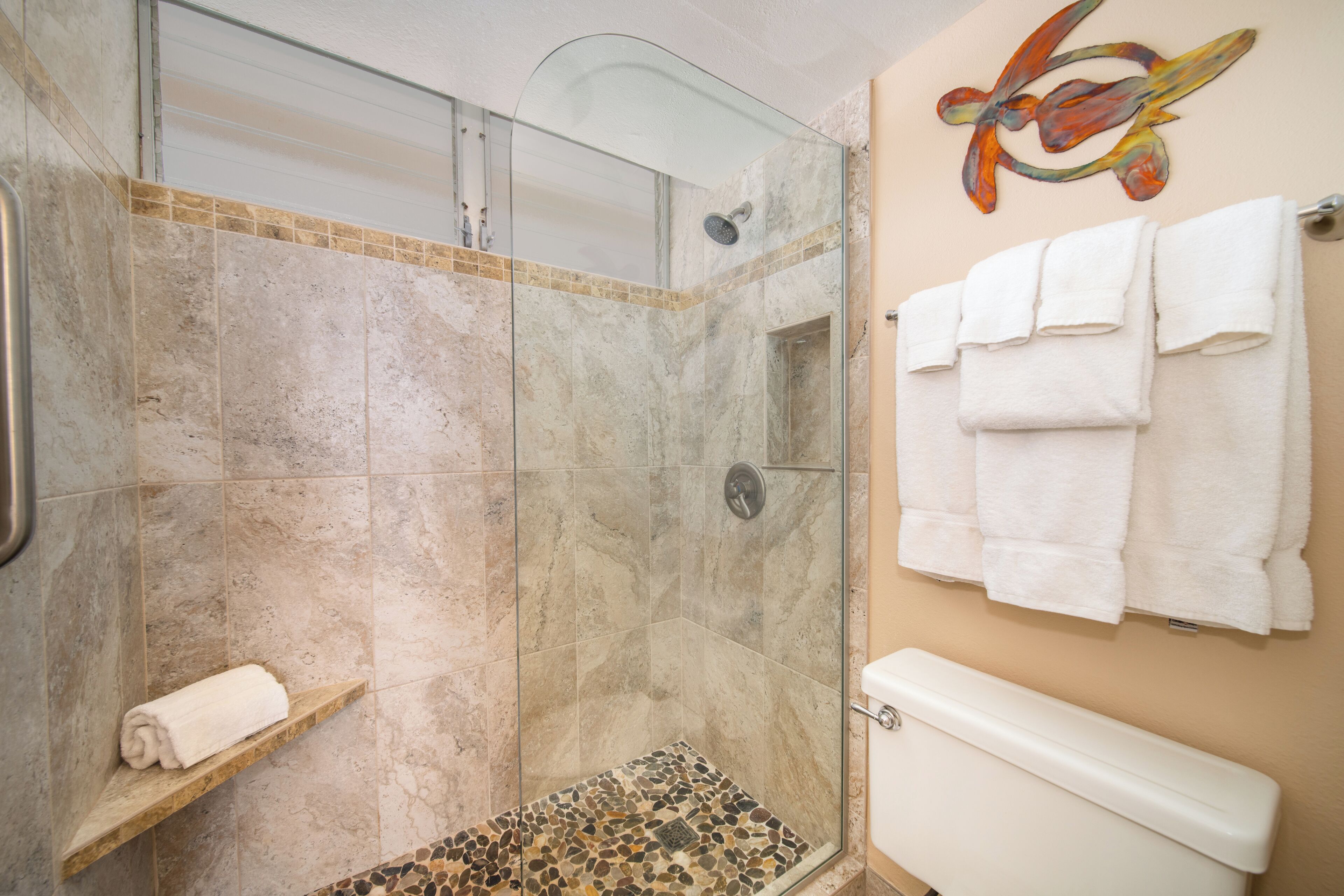 A bathroom with a glass-enclosed shower, a marble-tiled floor, and a toilet with a beige wall.