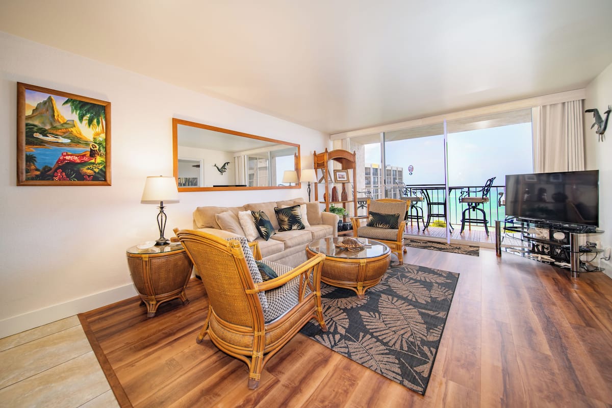 A living room with a sofa, two armchairs, a coffee table, a TV, and a balcony with a view.