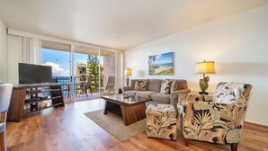 A modern living room with a flat-screen TV, a sofa, a coffee table, and a patterned armchair. - Royal Kahana Maui by OUTRIGGER (Lahaina)