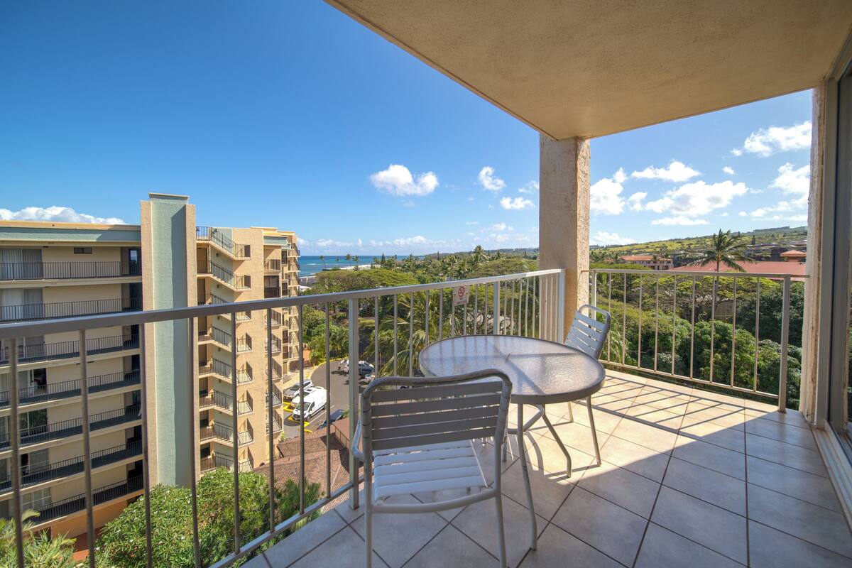 A balcony with a table and chairs, overlooking a residential area with buildings and a clear sky.