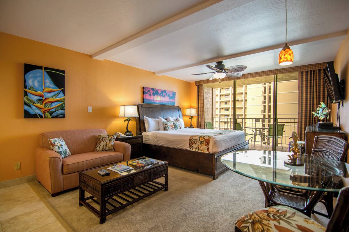 A hotel room with a bed, a sofa, a glass coffee table, and a dining table with chairs.