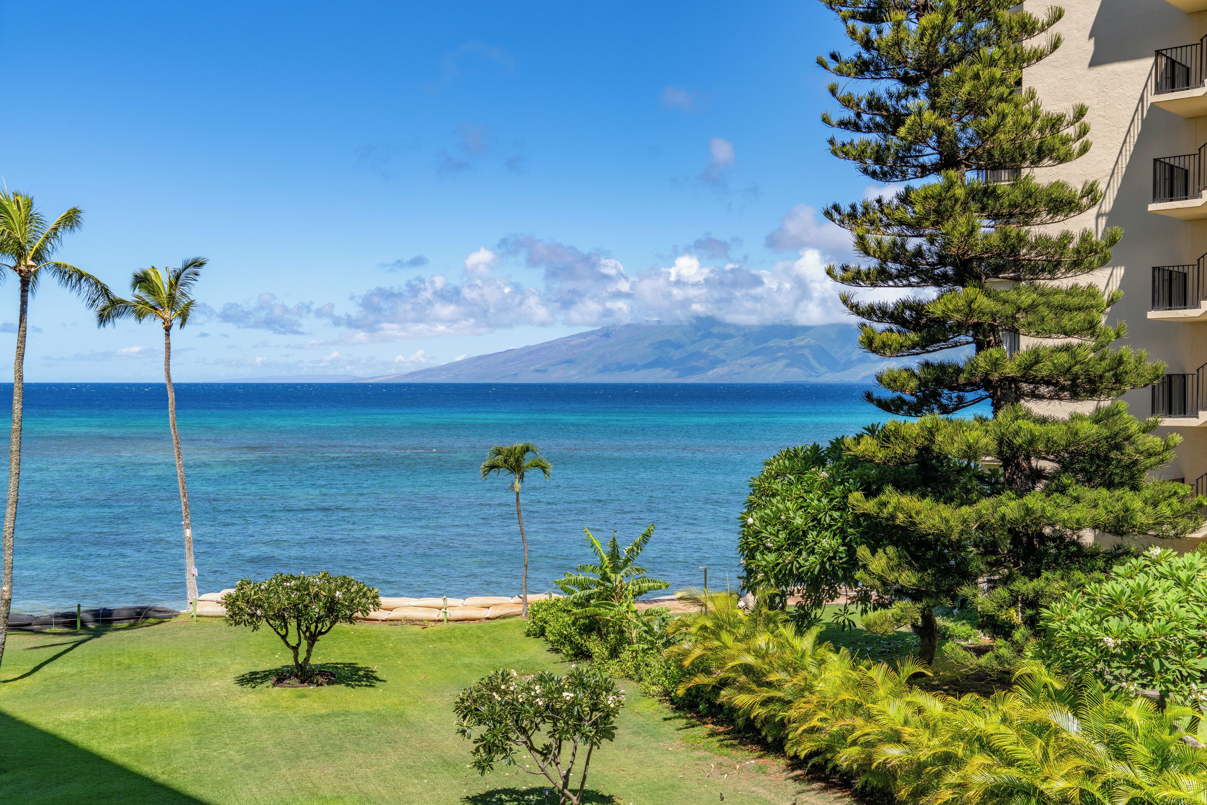 A coastal view with a clear sky, a mountain in the background, and a building with balconies overlooking the sea.