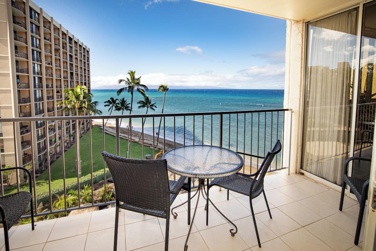 A balcony with a round table and four chairs, overlooking a beach and ocean.