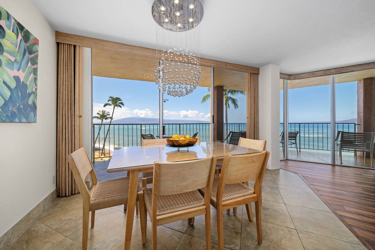 A dining area with a glass table, wooden chairs, and a view of the ocean.