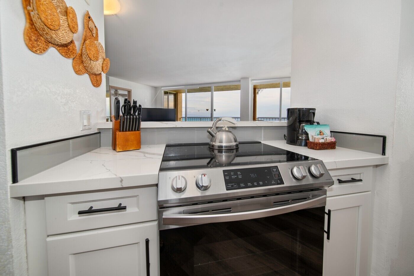 A modern kitchen with a gas stove, oven, and a view of the sea through large windows.
