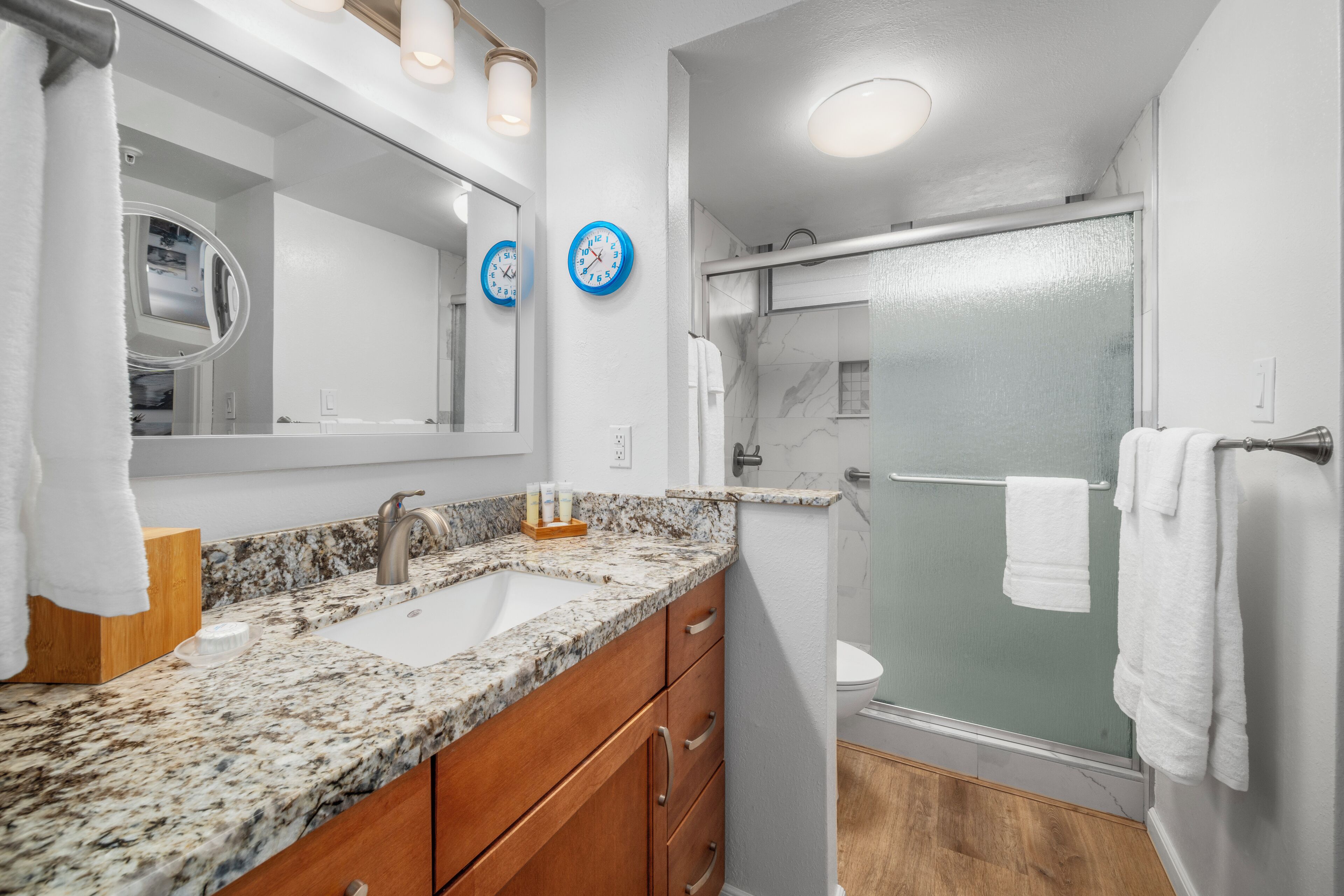 A modern bathroom with a granite countertop sink, wooden vanity, a large mirror, and a glass-enclosed shower.