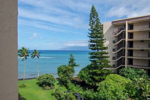 Vista de un hotel con balcón que da a una playa con palmeras y un cielo azul despejado.