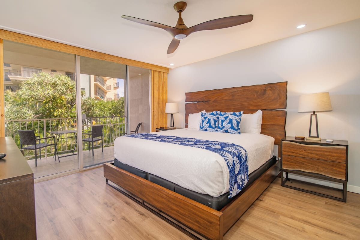 A modern bedroom with a large bed, wooden headboard, and a ceiling fan.