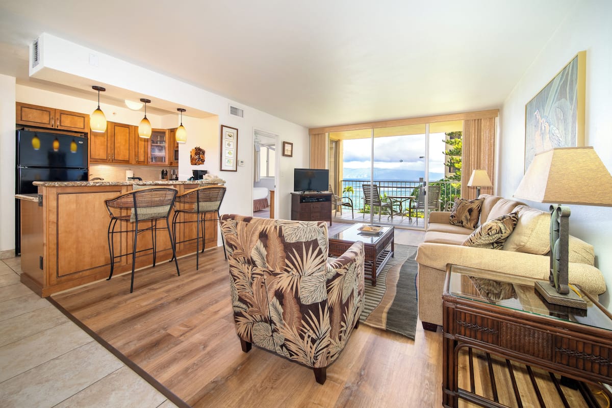 A spacious living area with a kitchen, a dining set, a sofa, and a balcony with a view.