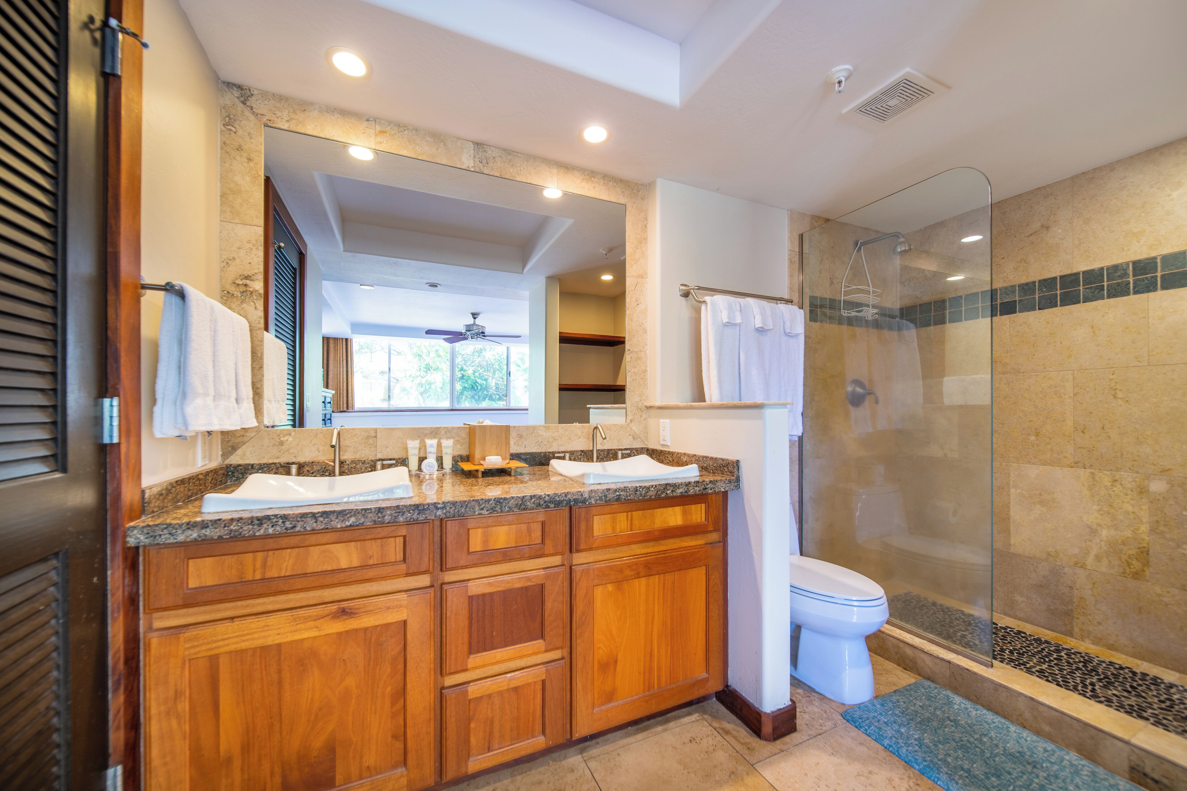 A bathroom with wooden cabinets, a granite countertop, a glass shower enclosure, and a white toilet.