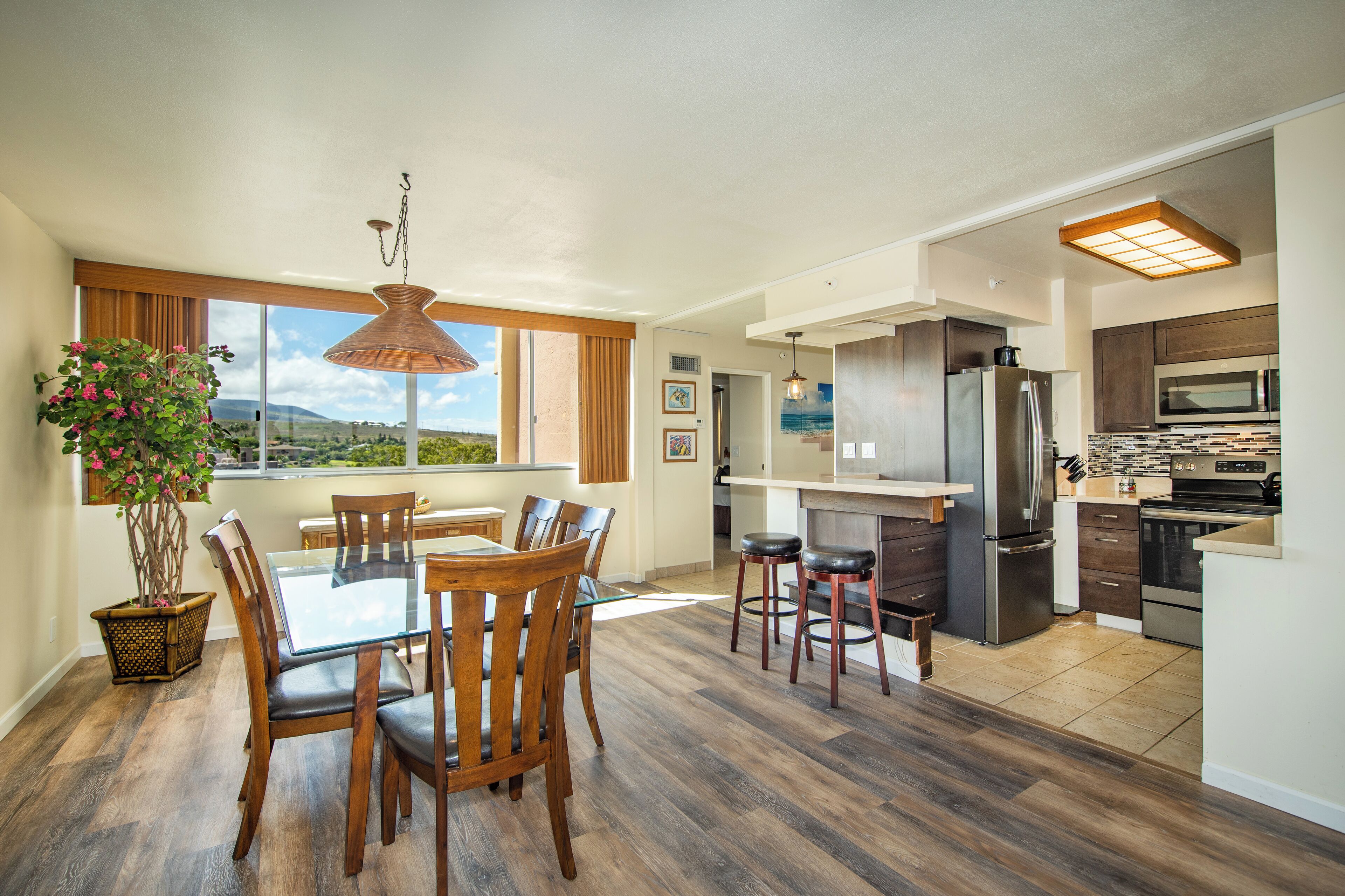 A modern kitchen with stainless steel appliances, wooden flooring, and a dining area with a glass table and chairs.