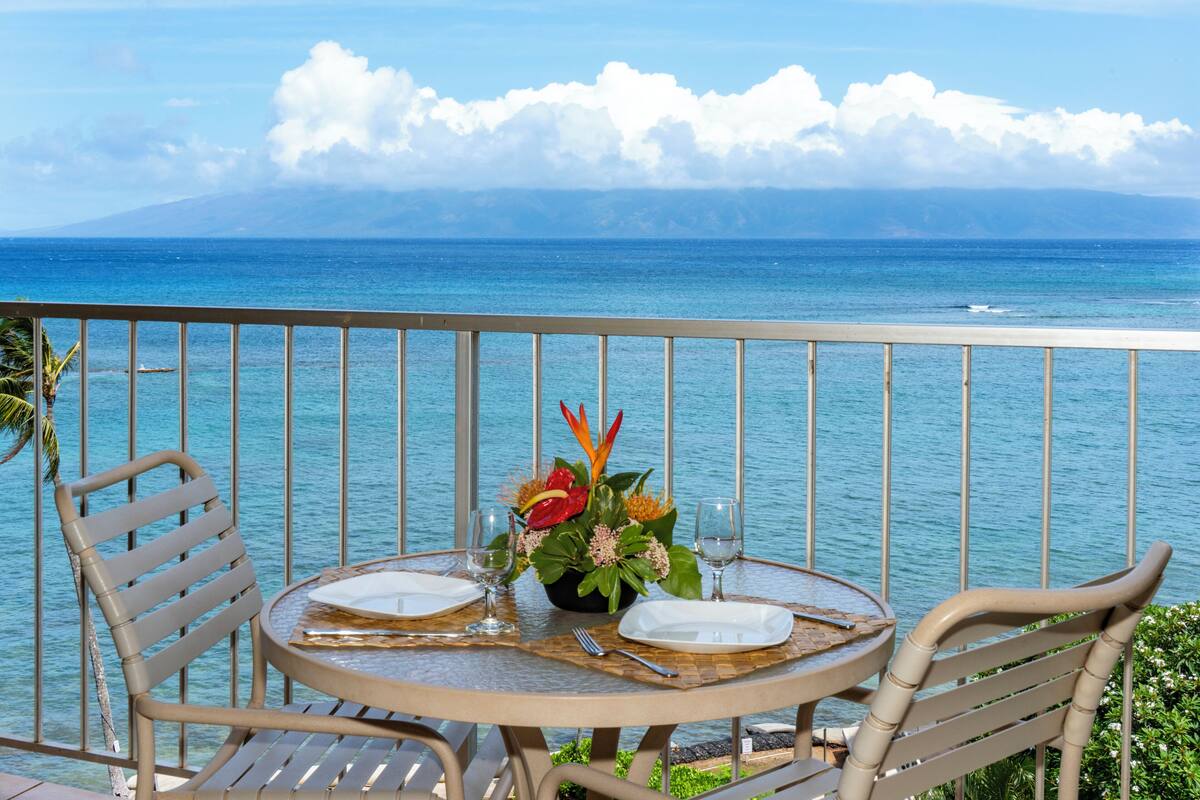 A round table with two chairs, a flower centerpiece, and a view of the ocean.