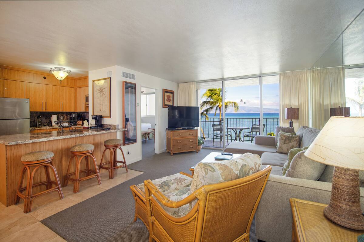 A spacious living area with a kitchen, a balcony with a view of the ocean, and a comfortable seating area with a sofa and chairs.