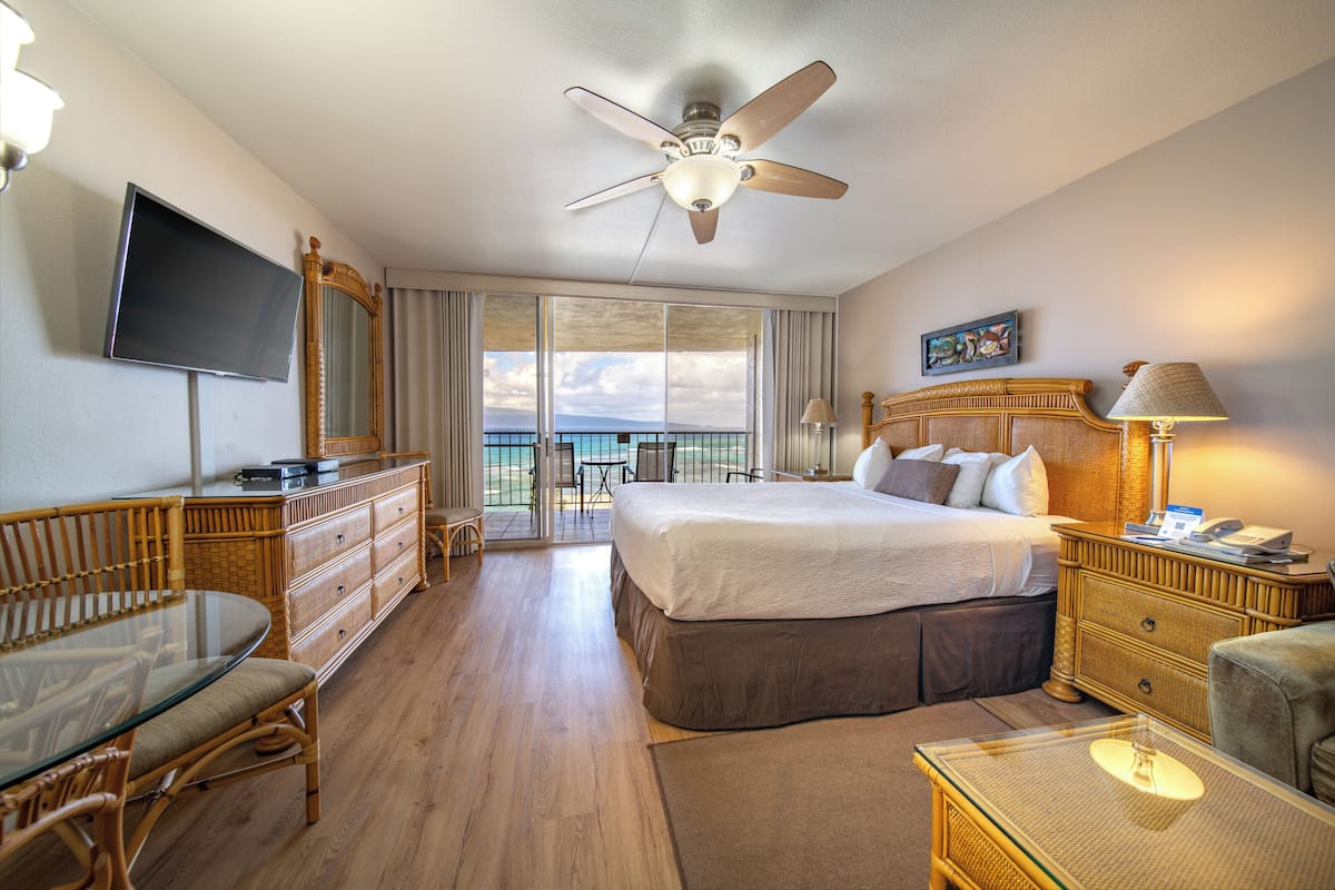 A hotel room with a bed, a television, a desk, a chair, a dresser, and a balcony with a view.
