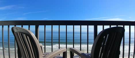 Two chairs facing a beach with a railing.