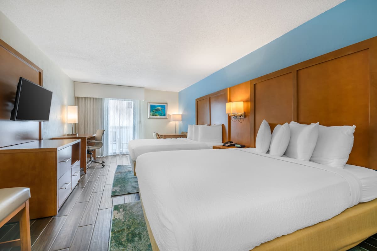 Ein Hotelzimmer mit zwei Betten, einem Schreibtisch, einem Fernseher und einem Gemälde an der Wand.
