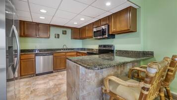 A kitchen with wooden cabinets, a stainless steel refrigerator, a built-in microwave, a dishwasher, and a granite countertop.