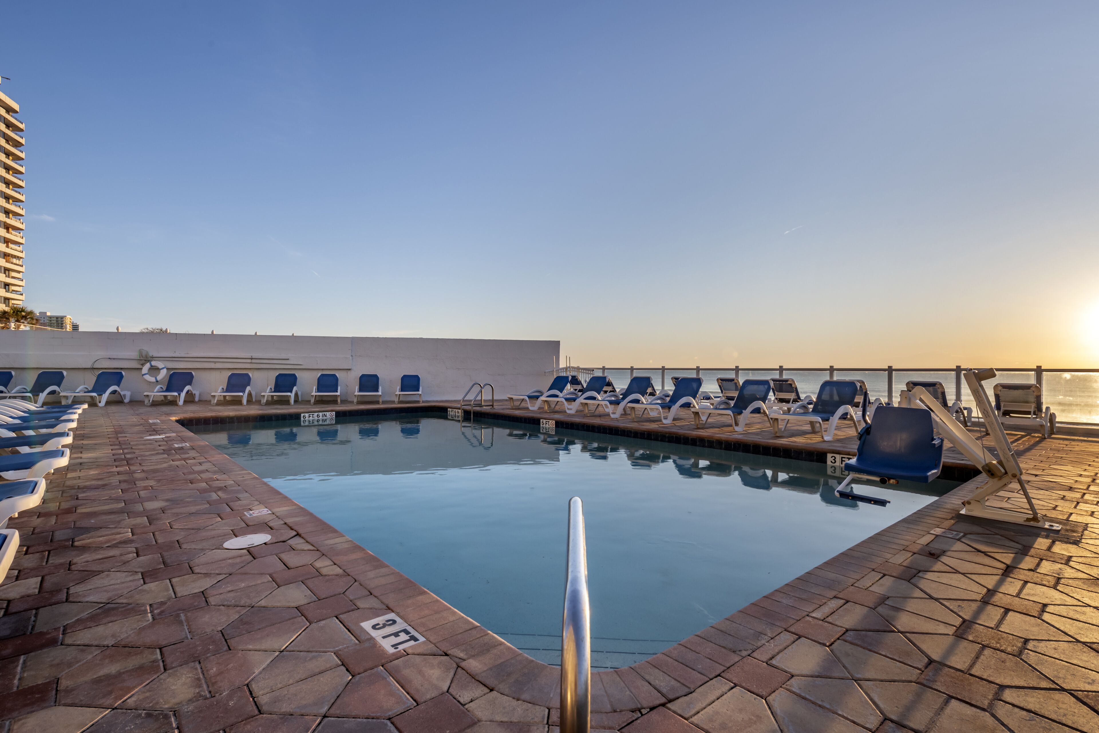 A rooftop pool with lounge chairs and a clear sky.