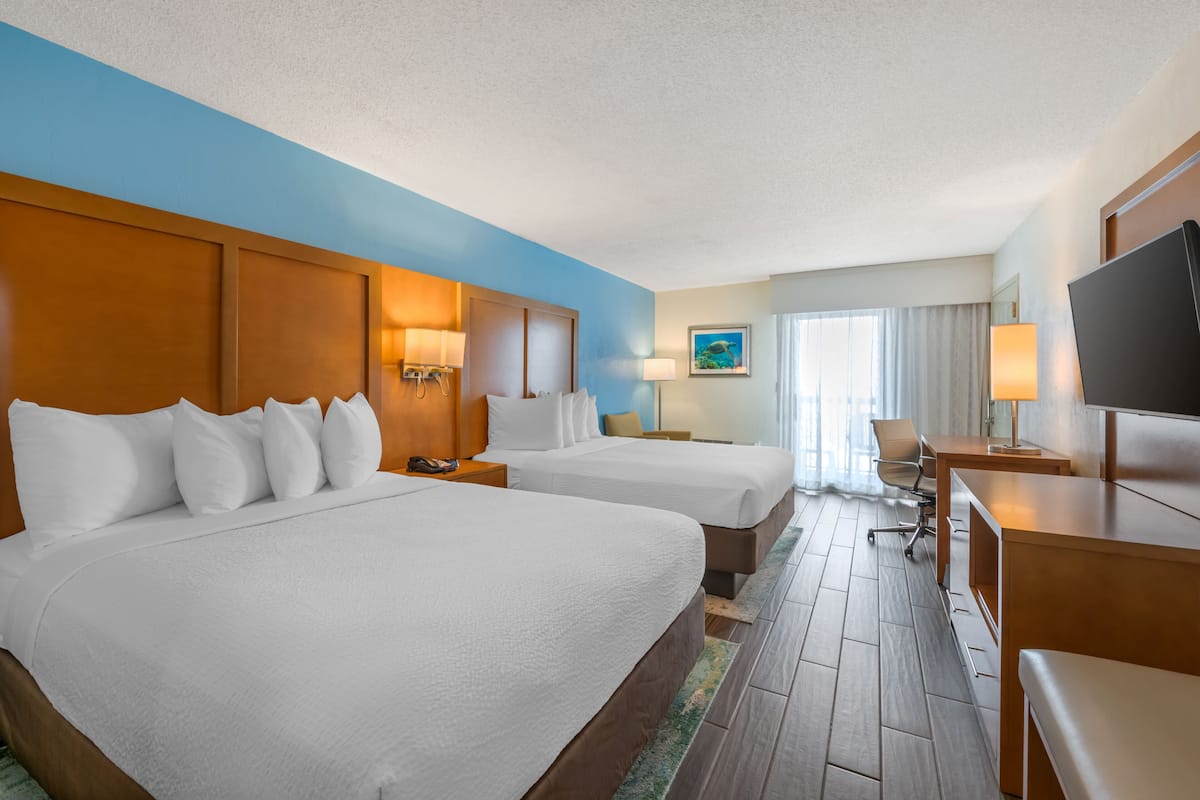 Ein Hotelzimmer mit zwei Betten, einem Schreibtisch, einem Fernseher und einem Gemälde an der Wand.