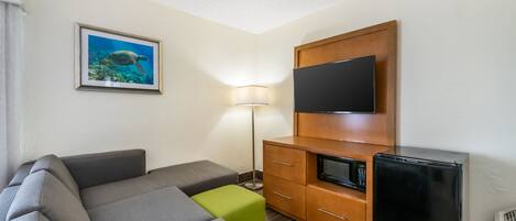 A modern living room with a sectional sofa, a flat-screen TV, a microwave, and a small refrigerator.