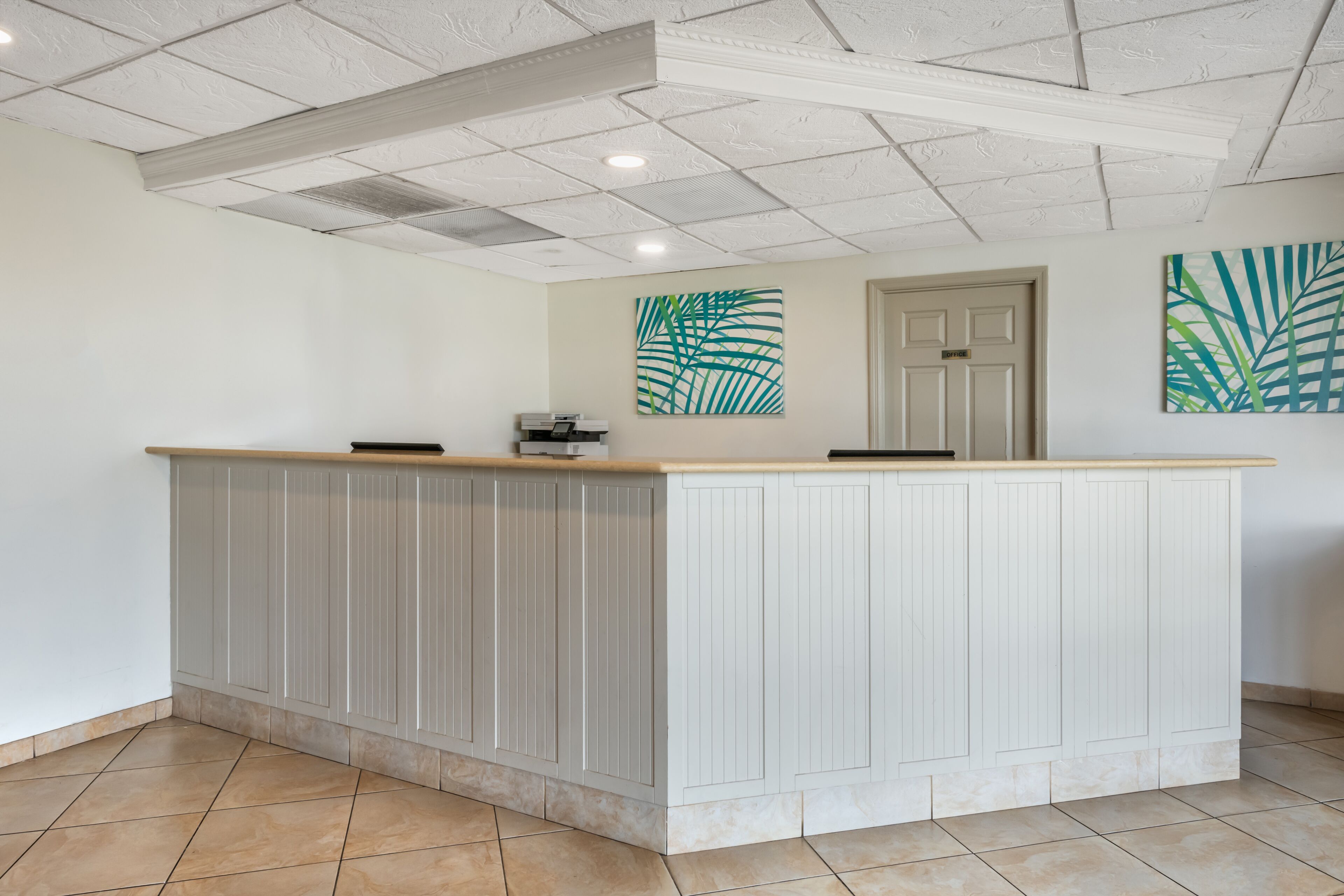 A reception area with a white reception desk, a door, and two large leaf-patterned wall art pieces.