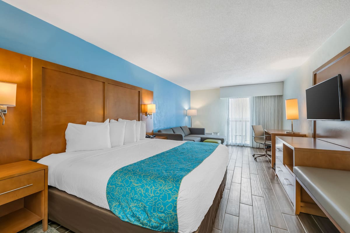 Ein Hotelzimmer mit einem großen Bett, einem Schreibtisch, einem Sessel, einem Fernseher und einem Fenster mit Vorhängen.