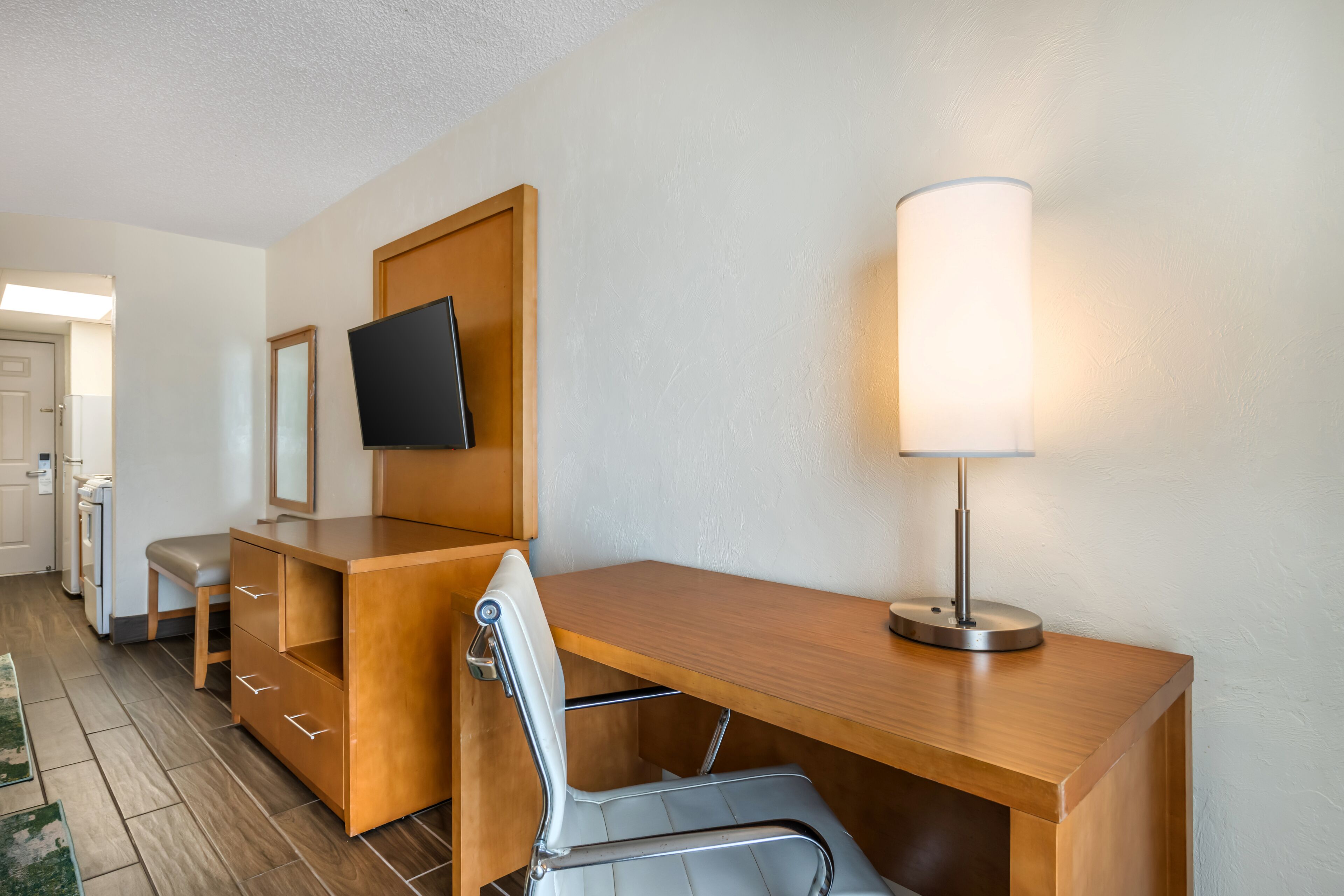 Ein Hotelzimmer mit Schreibtisch aus Holz, einem Sessel, einem an der Wand befestigten Fernseher und einer Nachttischlampe.