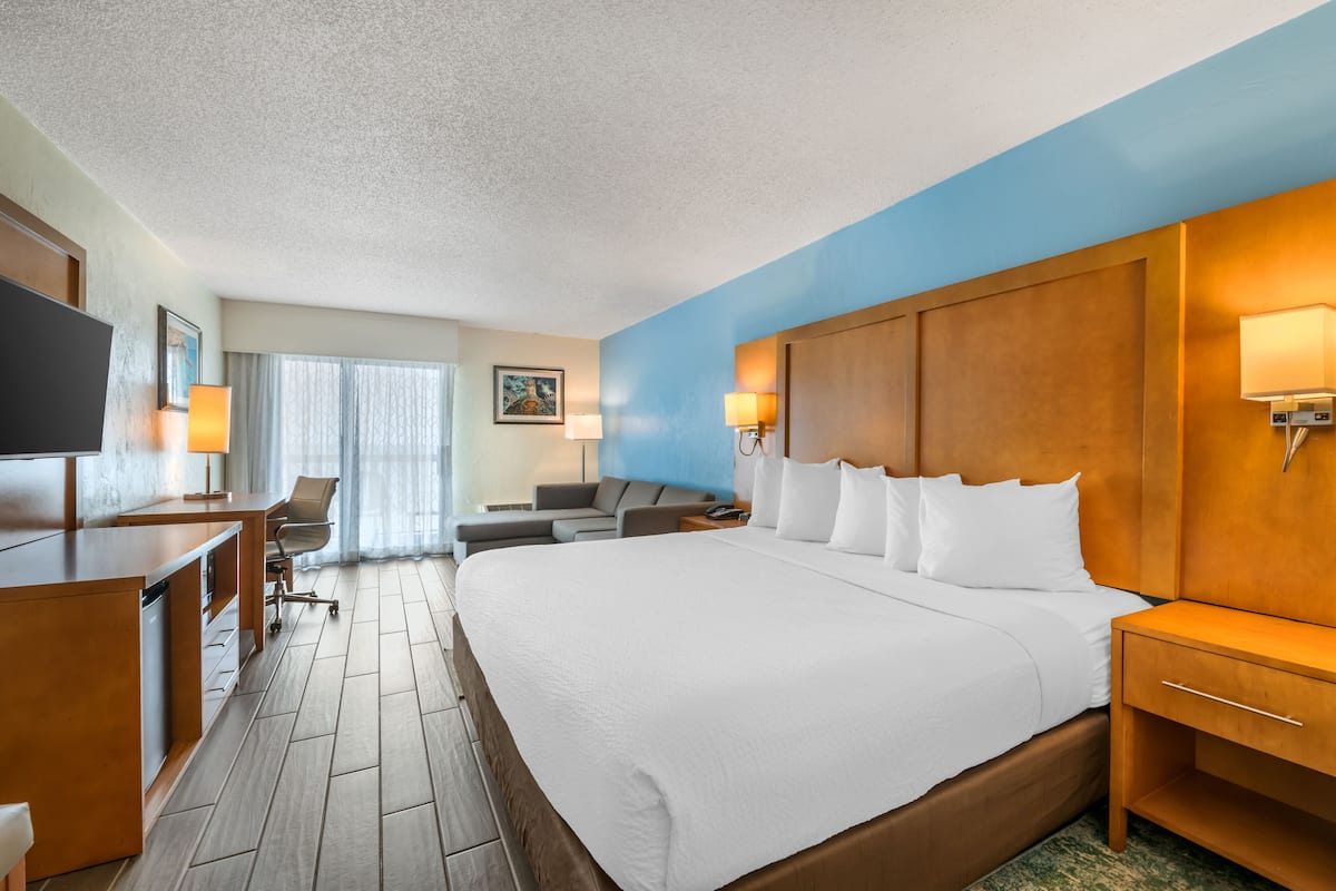 Ein Hotelzimmer mit einem großen Bett, einem Schreibtisch, einem Stuhl, einem Fernseher und einem Fenster mit Vorhängen.