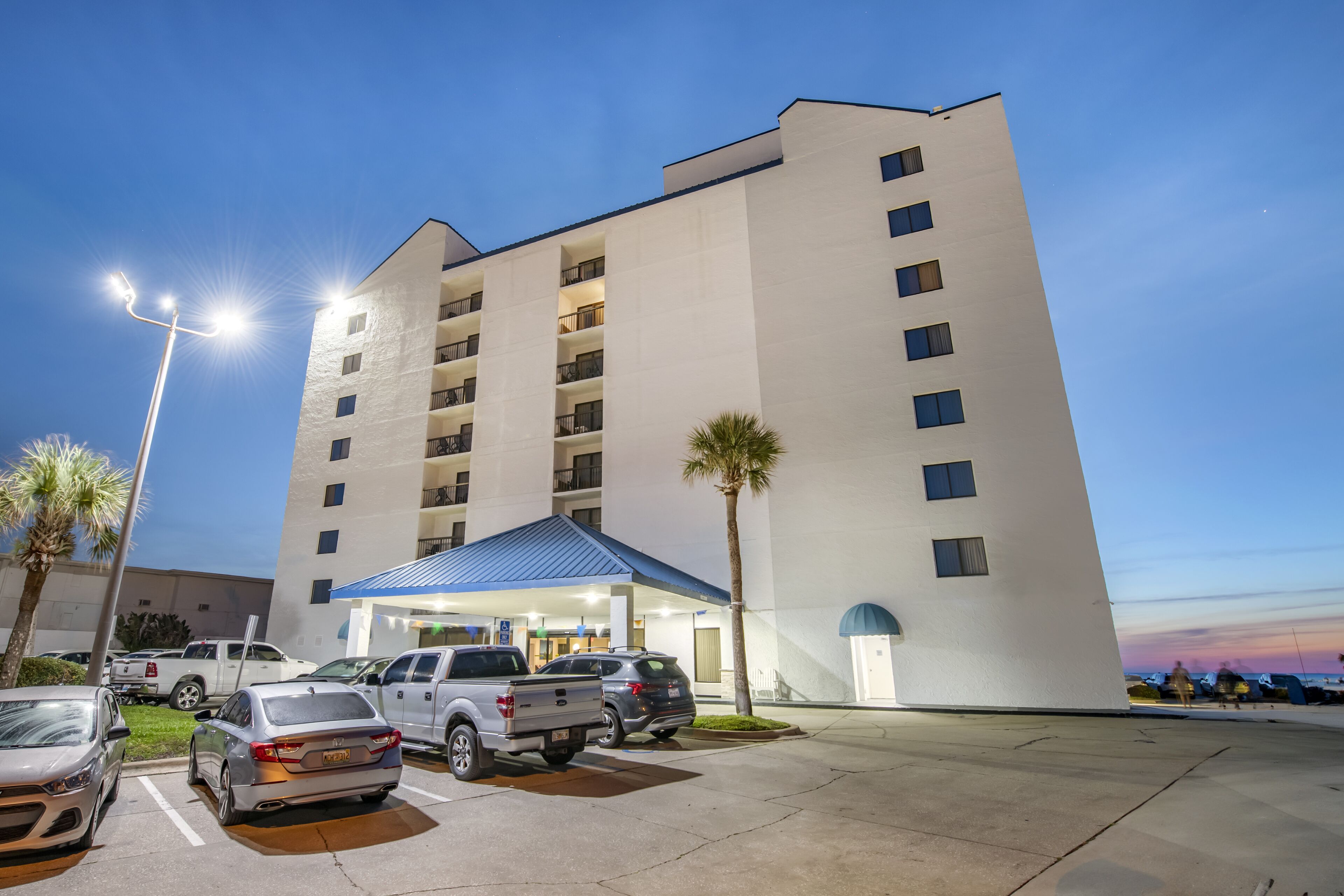 A multi-story hotel with a parking lot, a covered entrance, and a palm tree.