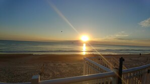 Una playa con barandilla en primer plano y el sol poniéndose sobre el océano.