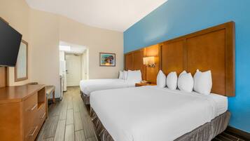 Une chambre d’hôtel avec deux lits, une commode en bois, un téléviseur et un tableau au mur.