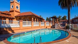 A swimming pool with a tiled deck, a building with a clock tower, and a palm tree.