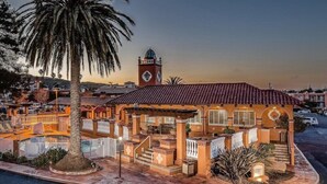 A hotel with a clock tower, a palm tree, and a pool area.