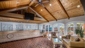 A spacious lobby with a high ceiling, wooden beams, a patterned floor, a reception desk, seating area, and large windows.