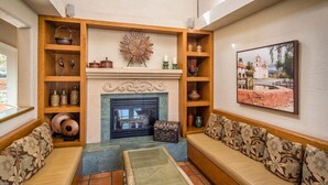 Een woonkamer met een open haard, houten planken, een bank en een glazen salontafel.