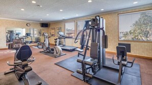 Een sportschool met diverse fitnessapparaten, grote ramen en een klok aan de muur.