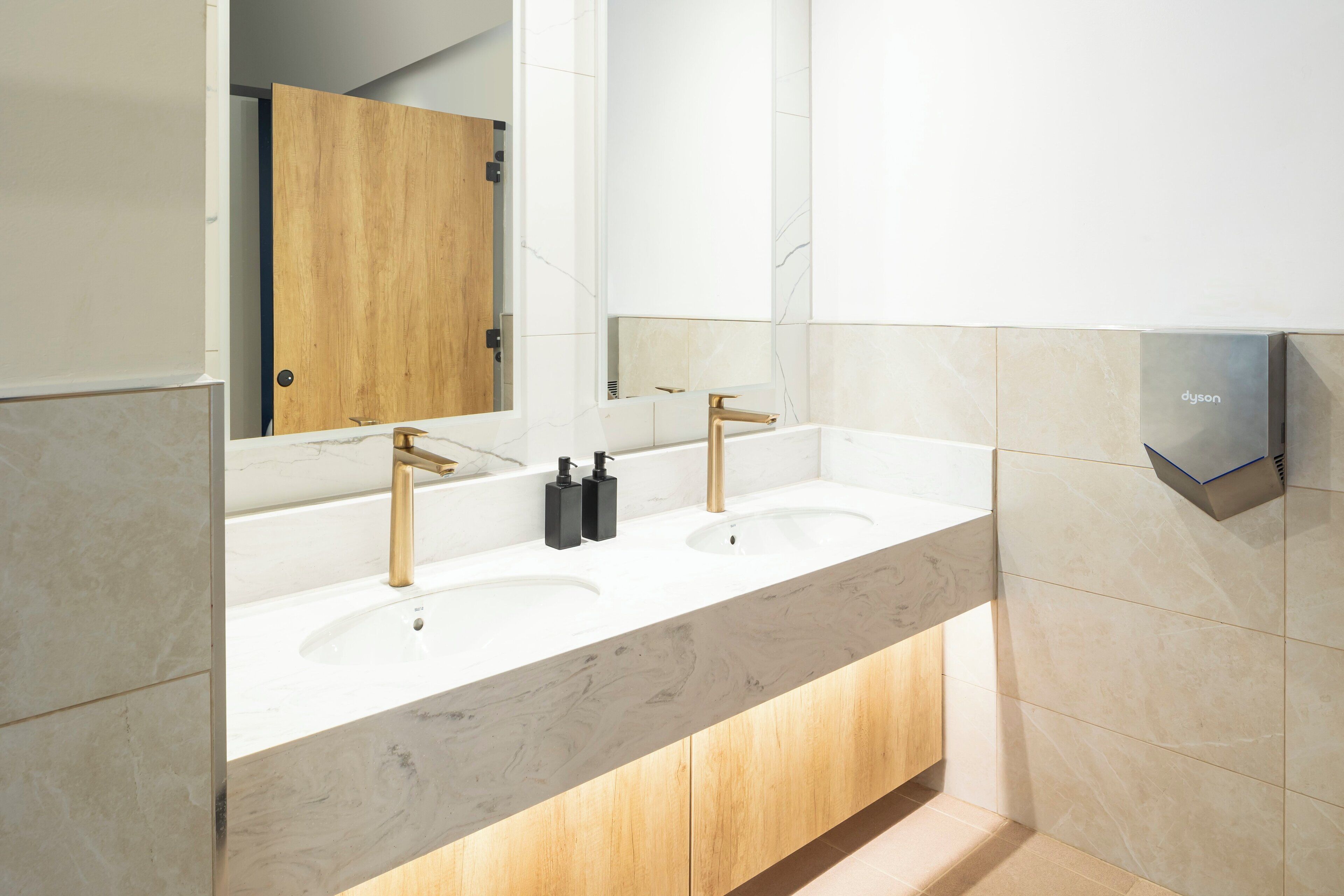 Un baño moderno con dos lavamanos, una puerta de madera y un espejo.