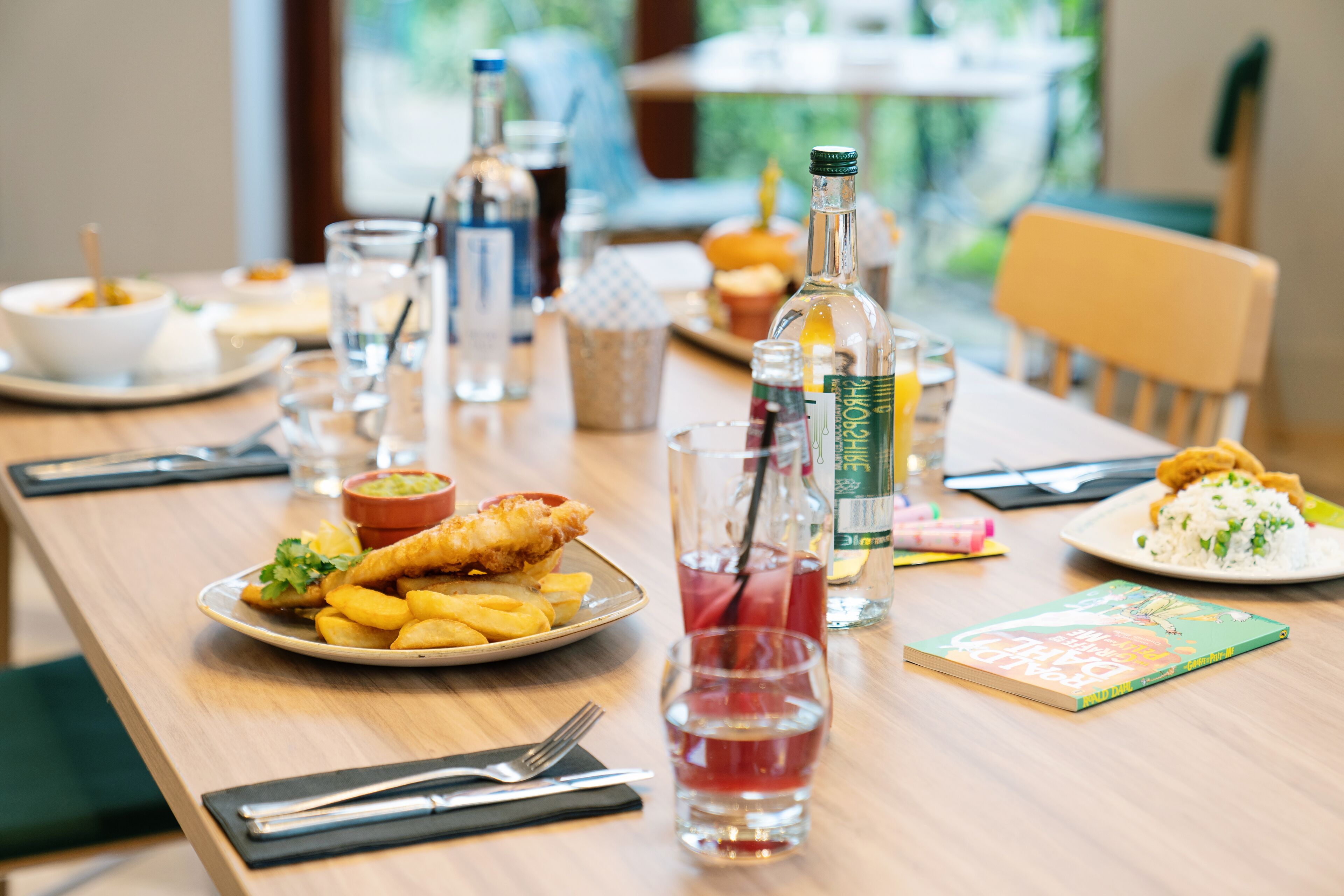 A dining table with plates of food, glasses, and bottles.