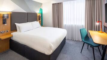 A hotel room with a large bed, a desk, a chair, and a TV.