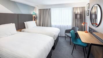 Quarto de hotel com duas camas, uma escrivaninha, uma cadeira, um abajur e um espelho grande.