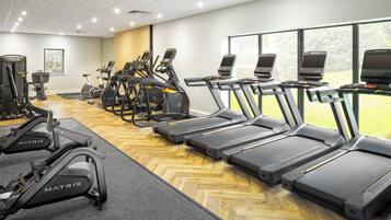 Un gimnasio con cintas de correr, elípticas y una máquina de remo.