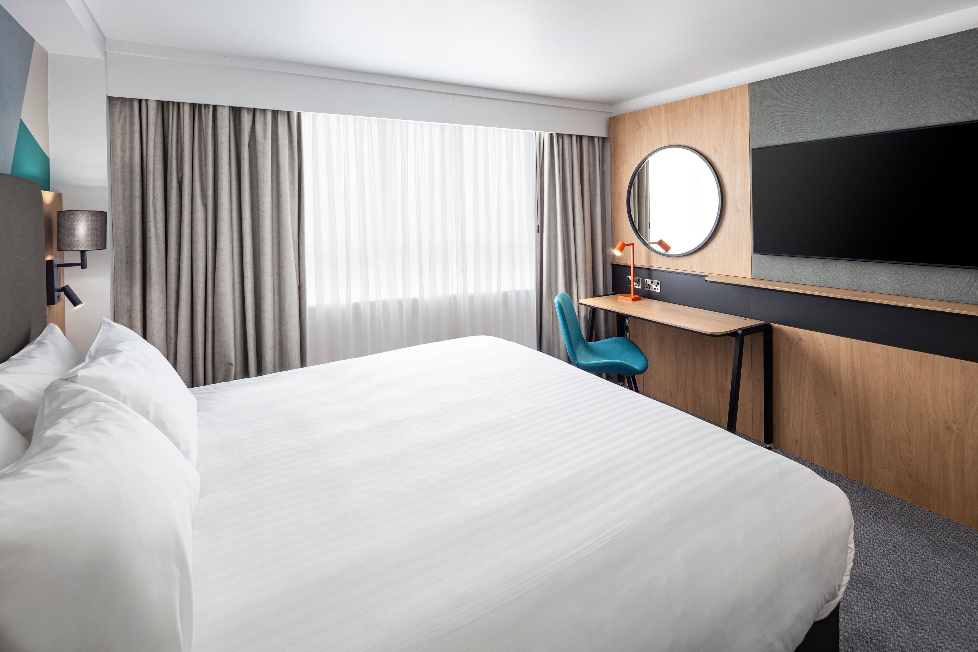 Una habitación de hotel con una cama grande, un escritorio con una silla, un televisor y una ventana con cortinas.