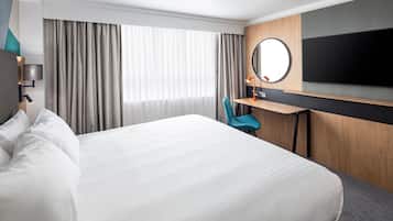 Una habitación de hotel con una cama grande, un escritorio con una silla, un televisor y una ventana con cortinas.