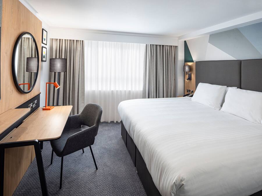 A hotel room with a bed, a desk, a chair, a TV, and a window with curtains.