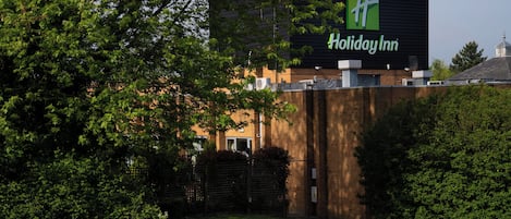A Holiday Inn hotel with a prominent green logo, surrounded by lush greenery and a well-maintained lawn.