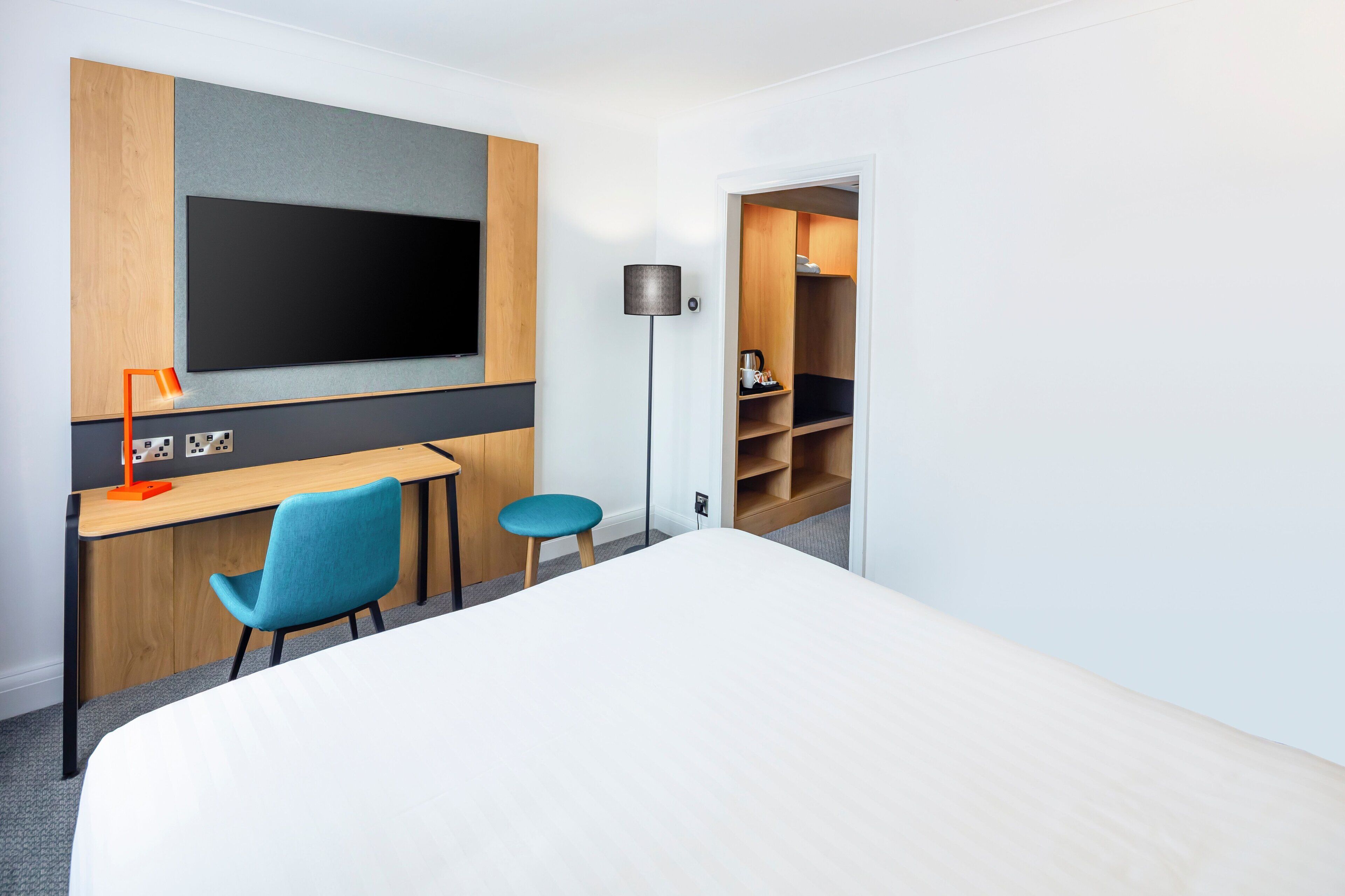 A hotel room with a bed, a desk with a chair, a TV, and a wardrobe.