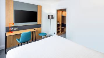 A hotel room with a bed, a desk with a chair, a TV, and a wardrobe.